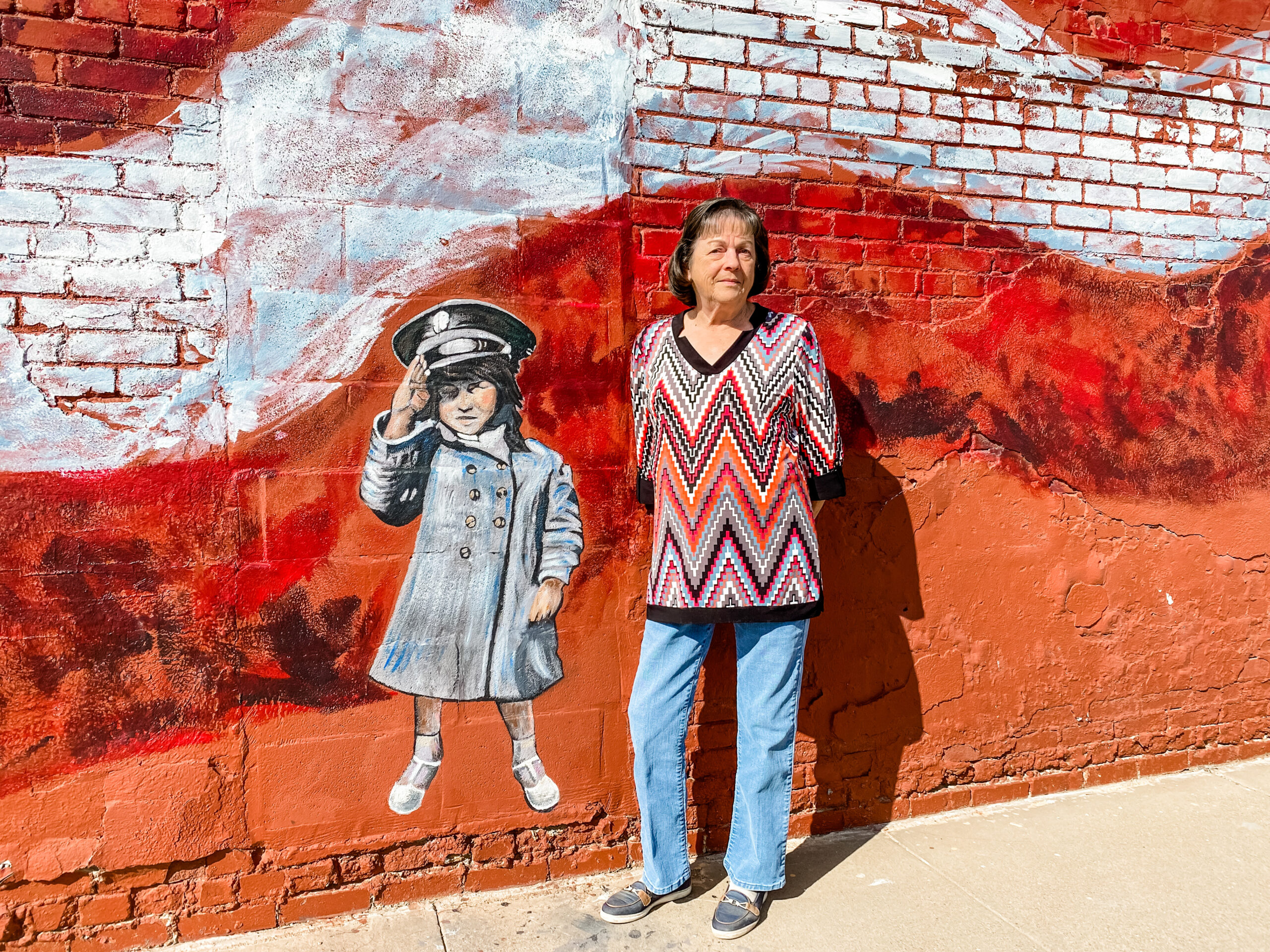 Shirley Mixon posing in front of the saluting girl murals as part of The Murals at 76067.